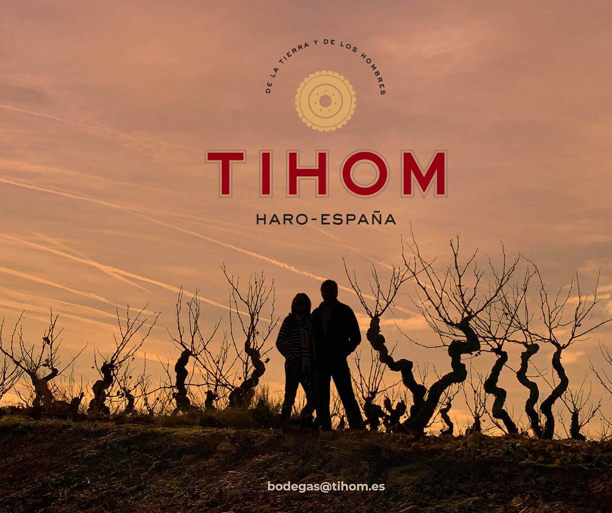 Two people in silhouette among old vines at sunset, under the Tihom name